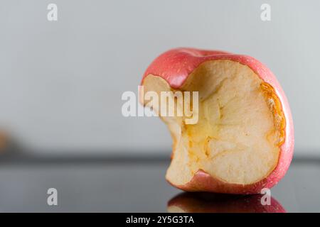 Eine Nahaufnahme eines gebissenen roten Apfels, der sein Inneres mit einer glatten Textur und hellen Farben zeigt. Der Apfel wird hochgradig auf eine reflektierende Oberfläche gelegt Stockfoto