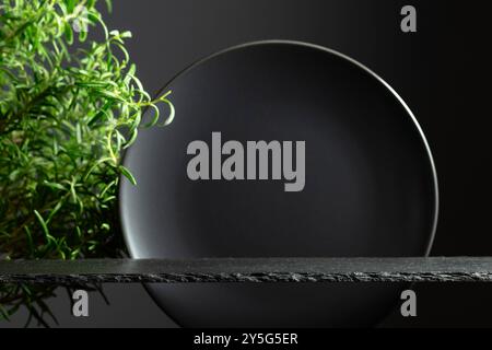 Schwarzes Steinpodium, schwarze Keramikplatte und Rosmarin-Zweige für Luxusproduktplatzierung. Minimaler Luxus. Kopierbereich. Stockfoto