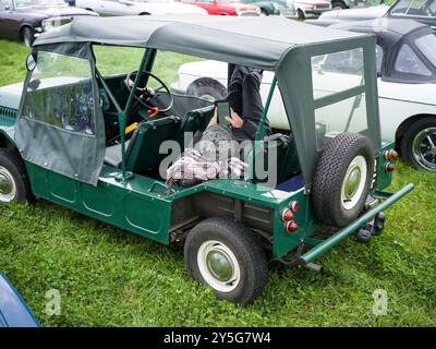 MINI MOKE MIT EINEM MANN, DER ENTSPANNT EIN BUCH AUF EINEM TABLET MIT STIEFELN AUF EINEM KLASSISCHEN SAINT MAWGAN DAMPFRALLYE LIEST Stockfoto