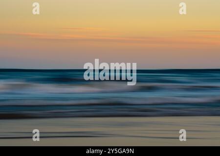 Sanfte Sonnenuntergänge verschwimmen über einer ruhigen Meeresküste. Stockfoto