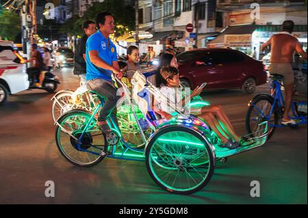 Eine Fahrrad-Rikscha bringt Touristen entlang der Straße in die Nachtstadt. Nha Trang, Vietnam - 21. Juli 2024 Stockfoto