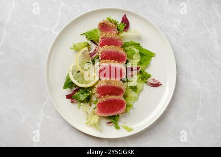 Bunte gebratene Thunfischscheiben sind kunstvoll auf einem Bett aus gemischtem Grün angeordnet. Frische Zitronenscheiben verbessern die Präsentation und machen sie zu einem Appetialin Stockfoto