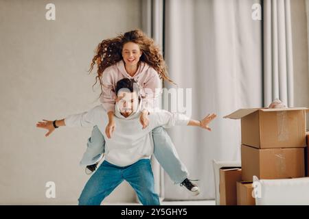 Glückliches junges Familienpaar, Mann und Frau, die spielen und genießen, nachdem sie Kartonschachteln in eine neue Wohnung gebracht haben. Stockfoto