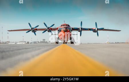 Orangefarbene an-12-Kamera. Hellgelbe Linie, die zu Turboprop-Flugzeugen führt, die auf dem Flughafenvorfeld abgestellt sind. CAVOK Air (UR-CSI) Frachtflugzeug. Stockfoto