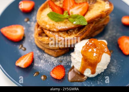 Französischer Toast garniert mit Erdbeeren und Minze, mit Eis und Karamellsauce auf einer blauen Platte. Leckeres und gesundes Frühstück. Nahaufnahme. Hoch q Stockfoto