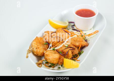 Goldene gebratene Garnelen, serviert mit frischen Limettenscheiben und Dippsoße, garniert mit Salat Stockfoto