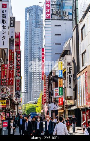 Blick auf Chuo dori, eine enge Einkaufsstraße in Shinjuku mit dem riesigen Tokyo Metropolitan Gebäude am Ende, das den Himmel an einem sonnigen Tag erfüllt. Stockfoto