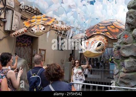 Barcelona, Spanien - 21. August 2024 Personen fotografieren am Eingang einer geschmückten Straße. Sie laufen durch den Gracia Bezirk in Fiesta de Gracia Stockfoto