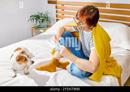 Frau, die mit ihrem Hund Jack Russell Terrier auf dem Bett sitzt und ein Digitalthermometer hält, die Körpertemperatur messen. Stockfoto