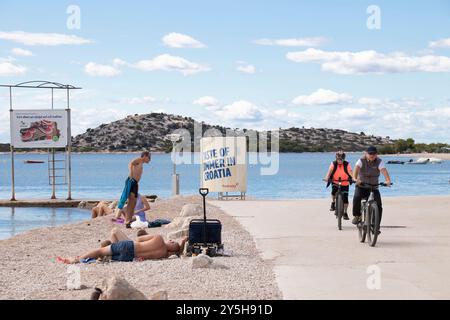 Vodice, Kroatien - 14. September 2024: In der Nebensaison schwimmen und Fahrrad fahren Menschen am Strand Stockfoto