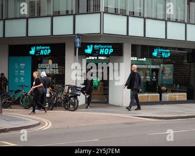 Fahrradfahrer versammeln sich vor dem Deliveroo Hop Lebensmittelgeschäft im Zentrum von London, Großbritannien Stockfoto