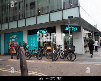 Fahrradfahrer versammeln sich vor dem Deliveroo Hop Lebensmittelgeschäft im Zentrum von London, Großbritannien Stockfoto