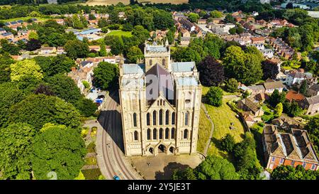 Blick aus der Vogelperspektive auf eine große historische Kathedrale, umgeben von üppigem Grün und einem malerischen Dorf. Die Kathedrale besticht durch eine komplexe Architektur und einen hohen spi Stockfoto