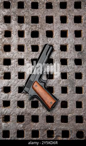 Schwarze Handpistole mit Holzgriff auf einem rostfreien Industriemetallgitter mit quadratischen Öffnungen. Eine robuste, kontrastreiche Aufnahme, die perfekt für Illustrationen geeignet ist Stockfoto
