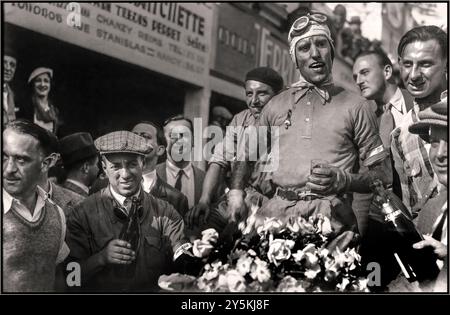 Tazio Nuvolari feiert seinen Sieg beim Großen Preis von Frankreich 1932 (am 3. Juli 1932 auf dem Reims-Gueux-Rundkurs) mit Blumen, Champagner und toller Fanfare. Nuvolari fuhr für Alfa Romeo in einem Tipo B „P3“, dominierte das Rennen und besiegte starke Konkurrenten wie Rudolf Caracciola. Dieser Sieg war bedeutend, da er Nuvolaris bemerkenswerte Fahrkünste und die technische Überlegenheit von Alfa Romeo demonstrierte. Stockfoto