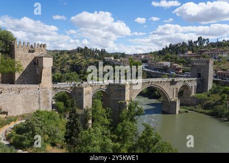 Alte Brücke über den Fluss in malerischer hügeliger Landschaft mit Festung und blauem Himmel mit Wolken, Puente de San Martin, Saint Martin's Bridge, Toledo, Tag Stockfoto