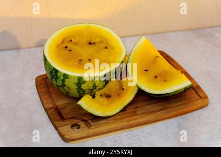 Herrliche gelbe Wassermelone, die elegant auf einem hölzernen Schneidebrett während eines sonnigen Nachmittagsversammels angeordnet ist Stockfoto