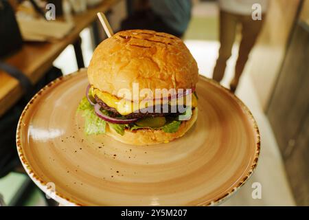 Ein köstlicher Cheeseburger, hoch gestapelt mit frischen Belägen, eingebettet auf einem rustikalen Teller, bereit, in einer gemütlichen Umgebung genossen zu werden Stockfoto