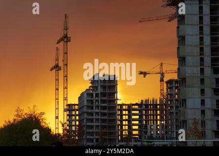 Während die Sonne untergeht, umhüllt ein markantes orangefarbenes Leuchten die Skyline und hebt Kraniche und unvollendete Strukturen hervor, die die Energie der Stadtentwickler zum Ausdruck bringen Stockfoto