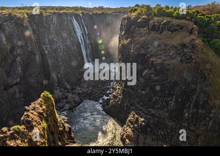 Eine atemberaubende natürliche Landschaft mit einem mächtigen Wasserfall, der in eine tiefe Flussschlucht stürzt, umgeben von felsigen Klippen mit üppigem Grün A Stockfoto