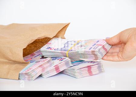 Die Hand einer Frau nimmt Päckchen ukrainischer Hrywnja heraus, die in einer Papiertüte auf weißem Hintergrund liegen, Geld und Gewinn, 200 Hrywnja in Päckchen Stockfoto