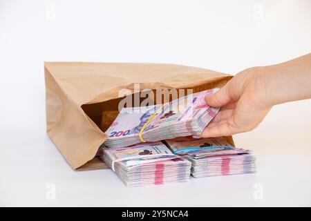 Die Hand einer Frau nimmt Päckchen ukrainischer Hrywnja heraus, die in einer Papiertüte auf weißem Hintergrund liegen, Geld und Gewinn, 200 Hrywnja in Päckchen Stockfoto