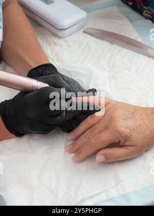 Eine Maniküre reinigt Nagelhaut und Farbreste von den Nägeln einer Frau mit einem elektrischen Nagelbohrer mit Flammengrat Stockfoto