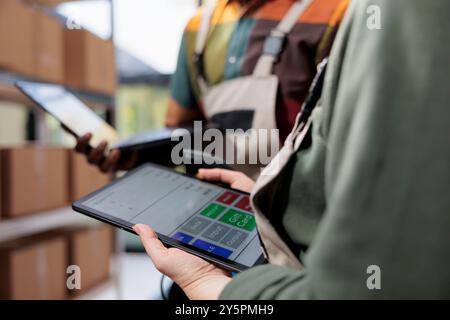 Lagerkollegen analysieren Lagerbestandsberichte auf Tablet-Computern, arbeiten an Kundenbestellungen, bevor Pakete im Lager versandt werden. Verschiedene Vorgesetzte, die sich die Checkliste für Waren ansehen. Nahaufnahme Stockfoto