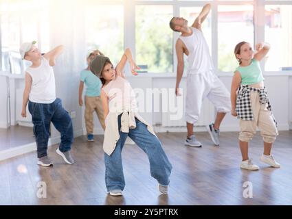 Glückliches Mädchen und Junge in lässigen Kleidern, die während des Trainings mit männlichem Lehrer Hip Hop tanzen Stockfoto