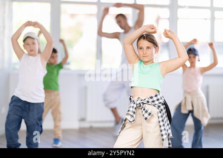 Glückliches Mädchen und Junge in lässigen Kleidern, die während des Trainings mit männlichem Lehrer Hip Hop tanzen Stockfoto