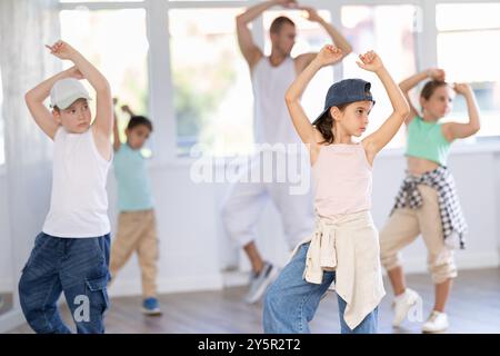 Glückliches Mädchen und Junge in lässigen Kleidern, die während des Trainings mit männlichem Lehrer Hip Hop tanzen Stockfoto