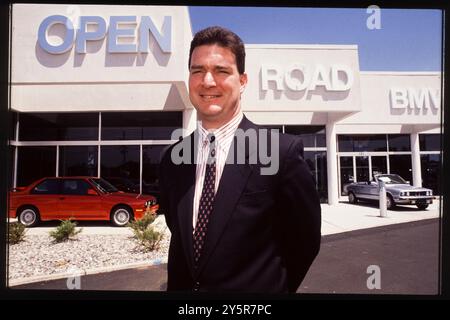 In den 1980er Jahren posiert ein Verkäufer selbstbewusst vor Open Road BMW in Trenton, New Jersey, und zeigt den Luxus und die Leistung von BMW Fahrzeugen, einschließlich des legendären roten E30 M3 und des Cabriolets. Stockfoto