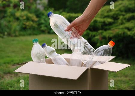 Recyclingkonzept. Mann, der Plastikflasche draußen in Pappkarton steckt, Nahaufnahme Stockfoto