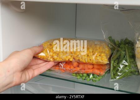 Eine Frau, die Plastiktüte mit gefrorenem Mais aus dem Kühlschrank nimmt Stockfoto