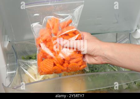 Eine Frau, die Plastiktüte mit gefrorener Karotte aus dem Kühlschrank nimmt Stockfoto