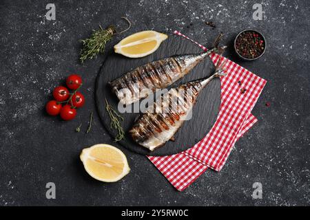 Köstliche gegrillte Makrele, Thymian, Zitrone und Tomaten auf dunklem, strukturiertem Tisch, flach gelegen Stockfoto