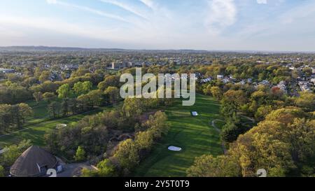 Blick aus der Vogelperspektive auf einen üppig grünen Golfplatz, umgeben von Wohngebieten und Bäumen an klaren Tagen. Stockfoto