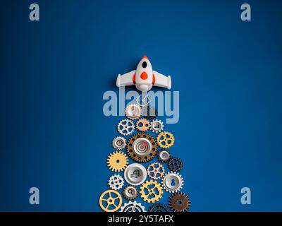 Weiße Raumschiff-Rakete fliegen mit vielen Zahnrädern als Jet Smoke auf blauem Hintergrund mit 3D-Strategie-Symbolen, minimaler Stil. Teamwork zu führen und zu managen Stockfoto