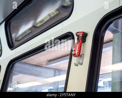 Roter Sicherheitshammer, Werkzeuge in der Nähe der Fensterscheibe im Zug oder Bus auf dem Baustellenhintergrund, Einsatz bei Unfällen. Stockfoto