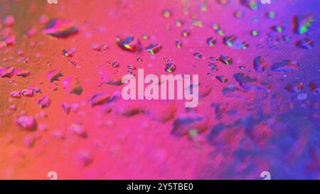 Regenbogentropfen. Nasses Glas. Defokussiertes lebendiges buntes Farbverlauf Neonlicht auf zerkratztem Distress Folienfilm Wasseroberfläche abstrakten Kunsthintergrund. Stockfoto