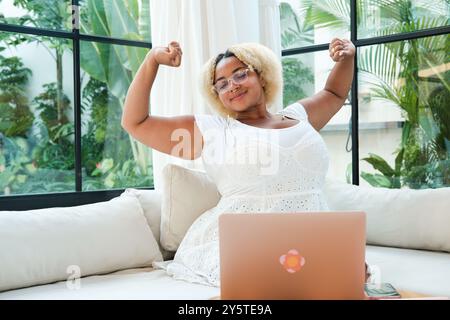 Afroamerikanische Kurvenfrau, die im Wohnzimmer sitzt und an einem Laptop arbeitet Stockfoto