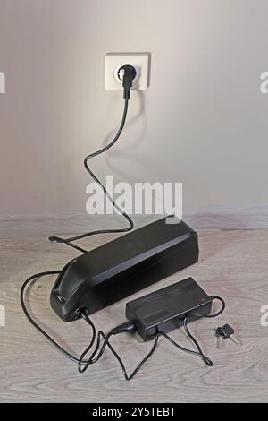 Laden der Fahrradbatterie über das Stromnetz im Haus. Steckdose im Zimmer mit eingeschaltetem Stecker. Umweltfreundlicher Transport. Stockfoto