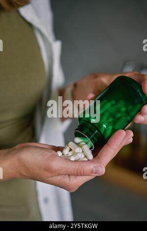 Nahaufnahme einer Frau, die weiße Kapseln aus grüner Flasche in die Hand gießt. Die Person nimmt Pillen oder Vitamine ein. Konzept der Nahrungsergänzungsmittel, Medizin oder Gesundheit c Stockfoto