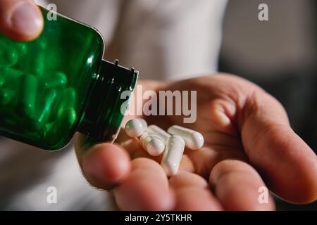 Nahaufnahme eines Mannes, der weiße Kapseln aus der grünen Flasche in die Hand gießt. Die Person nimmt Pillen oder Vitamine ein. Konzept von Nahrungsergänzungsmitteln, Medizin oder Gesundheitsauto Stockfoto