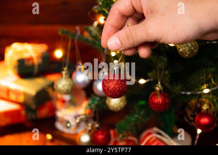 Männliche Hände, die rote Weihnachtskugel auf einen Weihnachtsbaum legen, weihnachtliches Traditionskonzept Stockfoto