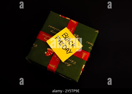 Grünes Weihnachtsgeschenk mit einer Nachricht auf gelbem Papier, auf der „Black Friday“ auf schwarzem Hintergrund steht, Weihnachtseinkaufkonzept Stockfoto