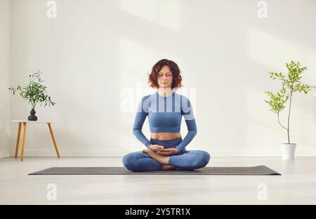Yogi konzentrierte weibliche Trainerin auf Matte mit überkreuzten Beinen und übte Yoga-Pranayama-Übungen Stockfoto