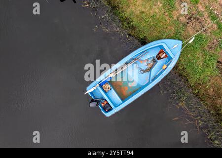 Ein kleines blaues Boot ruht ruhig am Ufer, was auf einen Tag zum Angeln hindeutet. Stockfoto