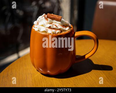 Herbstliche Kürbiswürze in einem Kürbisbecher mit Schlagsahne und Zimtstab. Ansicht schließen Stockfoto