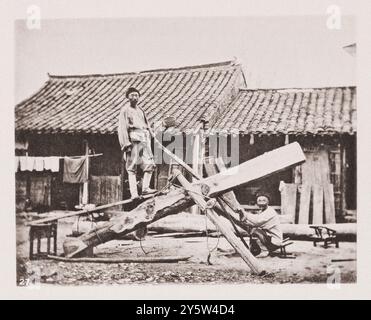 Vintage-Foto von chinesischen sägern bei der Arbeit. Illustrationen von Qing China, 1875 dort arbeitet der Zimmermann vor seinem Geschäft an einem grob behauenen Baum, der über einem Stativ steht, dessen Beine der Baum bildet (siehe Foto). Derselbe Mann kleidet das Holz, wenn er es zersägt hat, und macht es zu Stühlen und Tischen, außer in geschäftigen Städten, wo die Arbeit mehr geteilt ist. Die größten Sägen haben einfache Doppelgriffe, die durch die beiden Enden der Sägeblätter geführt werden. Sie sind auch quergeschnitten und so gesetzt, wie wir es sind. Außerdem gibt es eine Vielzahl von Sägen, die allmählich in ihrer Größe bis zum abnehmen Stockfoto